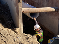 Worker assists in large drainage pipe installation in excavated worksite.